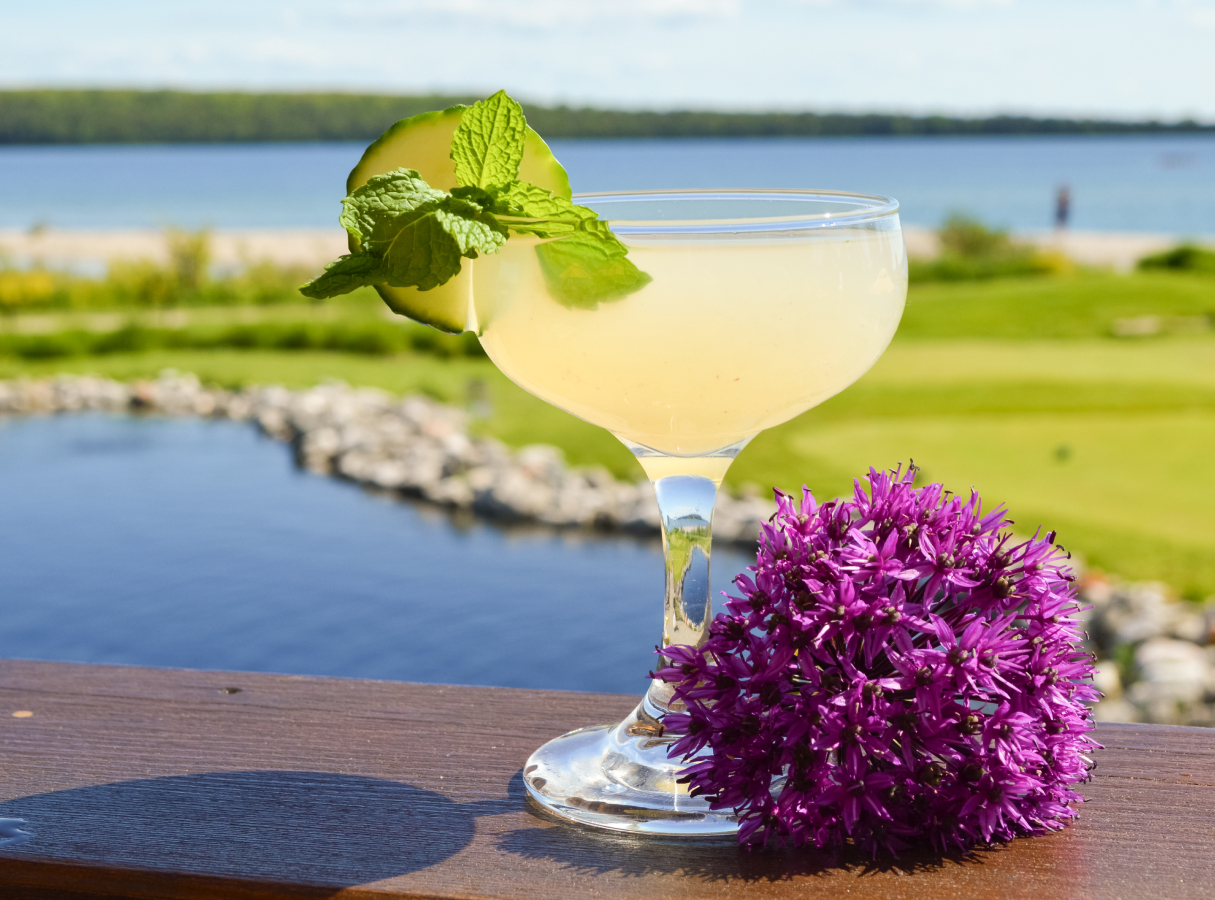 a glass of drink with a flower and a cucumber slice on top