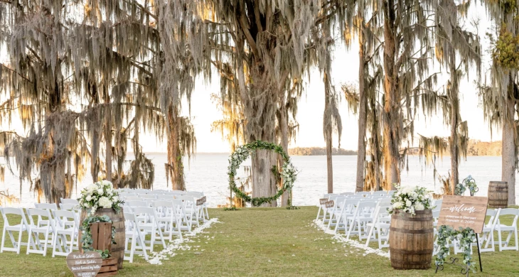 a wedding ceremony with white chairs and a wreath