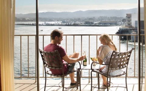 a man and woman sitting at a table with drinks on a balcony overlooking water