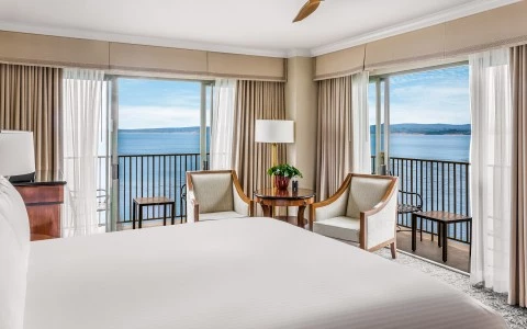 a room with a bed and chairs and a table with a balcony overlooking the ocean