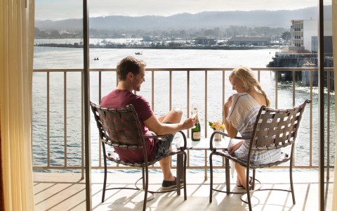 a man and woman sitting on a patio with a view of water and mountains
