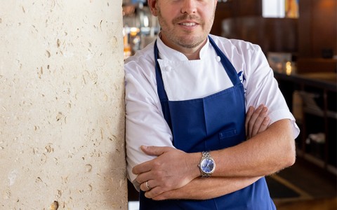 a man in a blue apron leaning against a wall
