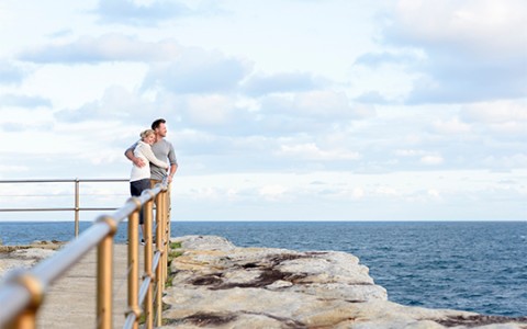 a man and woman hugging on a rock ledge overlooking the ocean