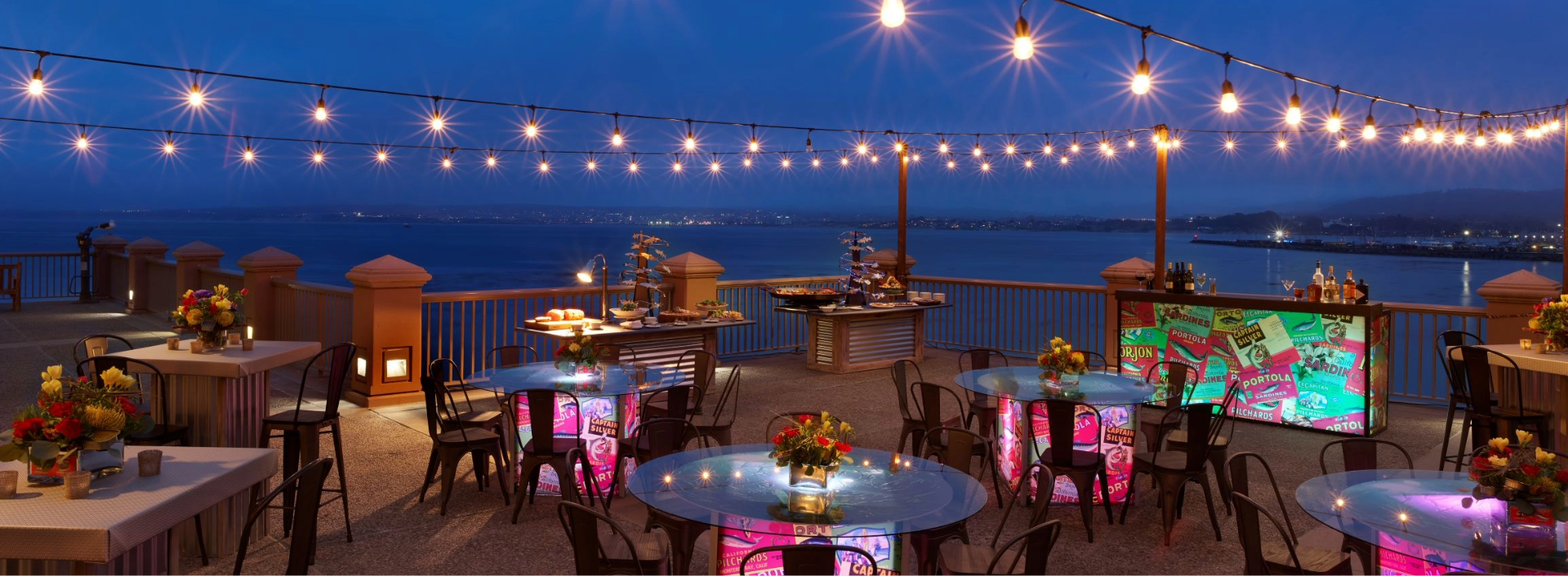 a table set up on a deck with lights and a body of water