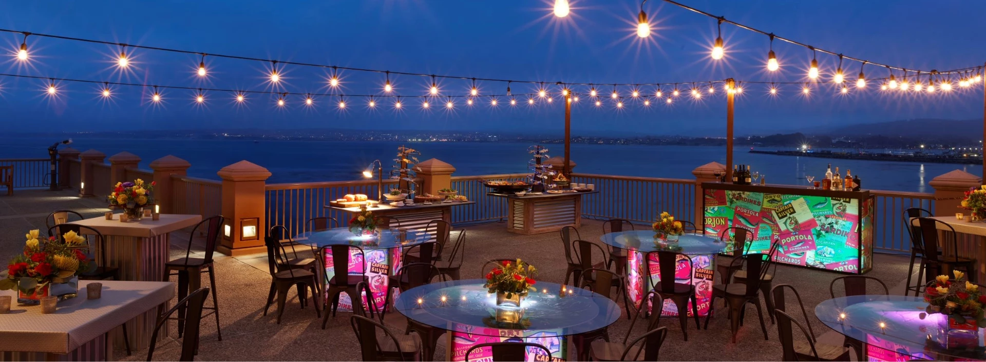 a table set up on a deck with lights and a body of water
