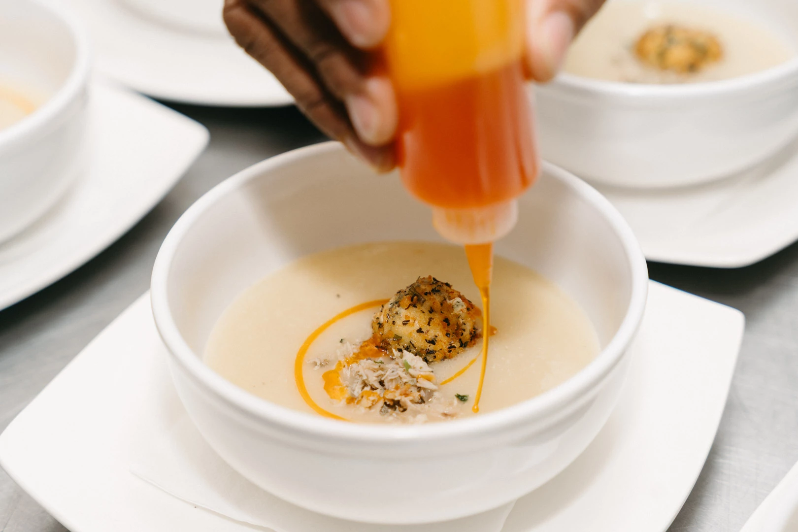 a person pouring a sauce into a bowl of soup
