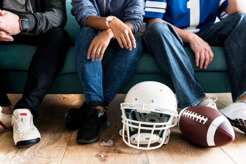 a group of people sitting on a couch with footballs and a helmet