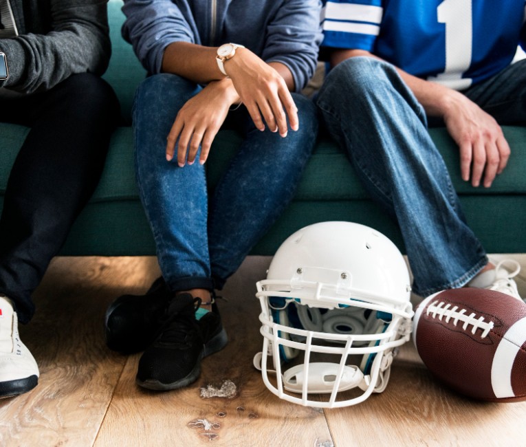 a group of people sitting on a couch with footballs and a helmet