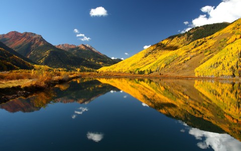 a lake with yellow trees and mountains in the background