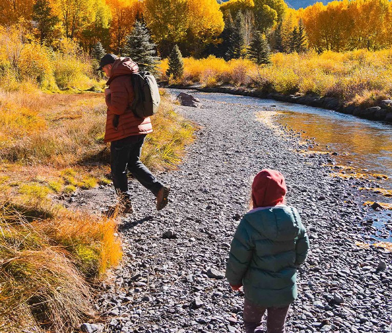 a man and child walking on a rocky path with yellow trees