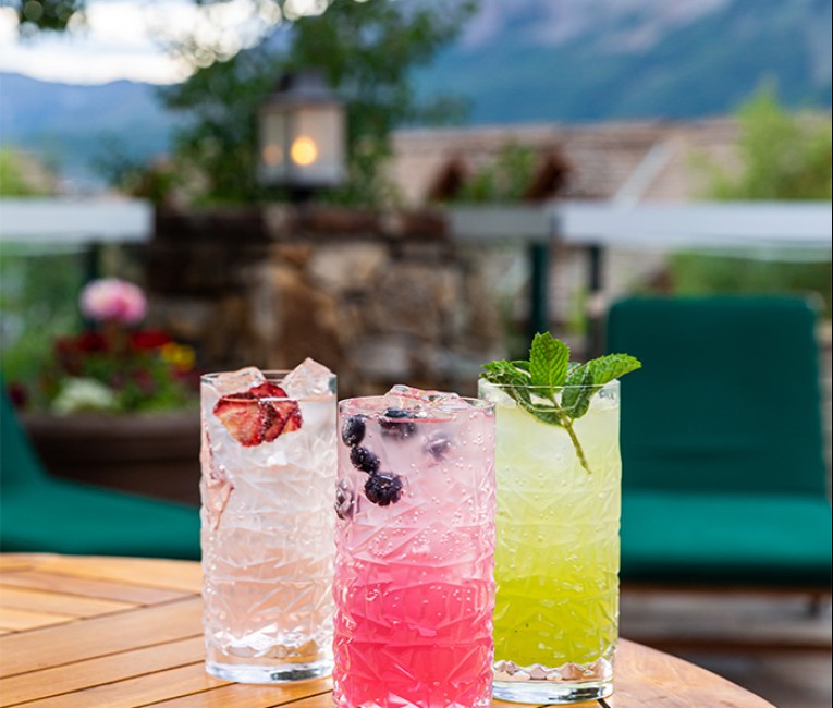three colorful cocktails on a table near the pool with mountains in the distance