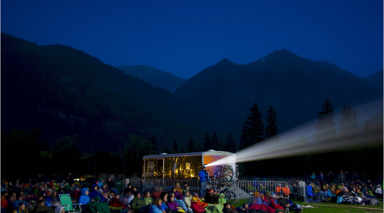 a group of people sitting on a lawn with a light projector
