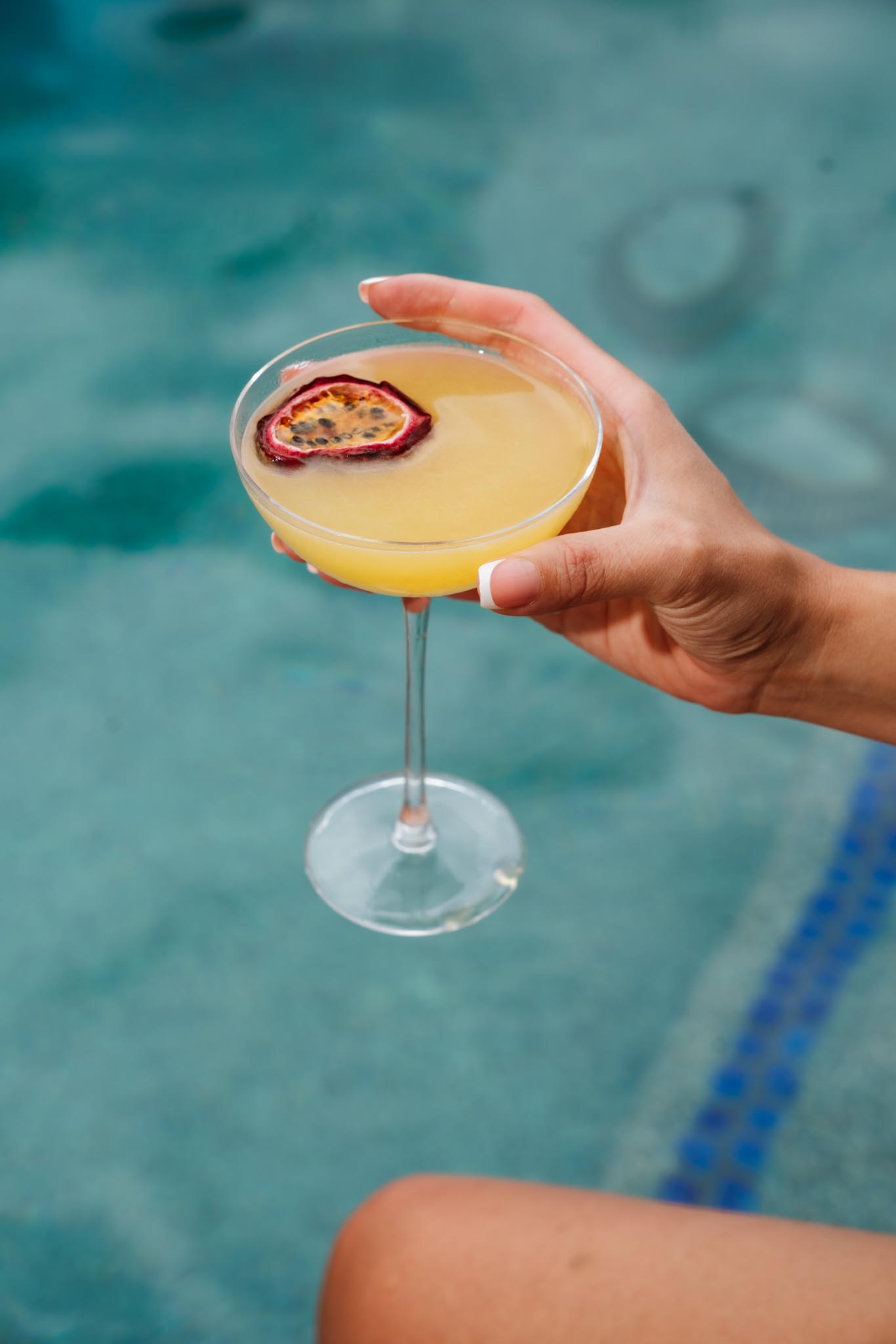 a hand holding a glass of yellow liquid with a passion fruit slice