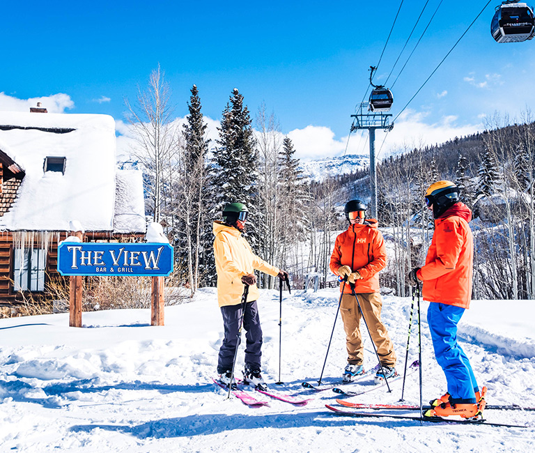the view bar and grill with three skiers standing near it