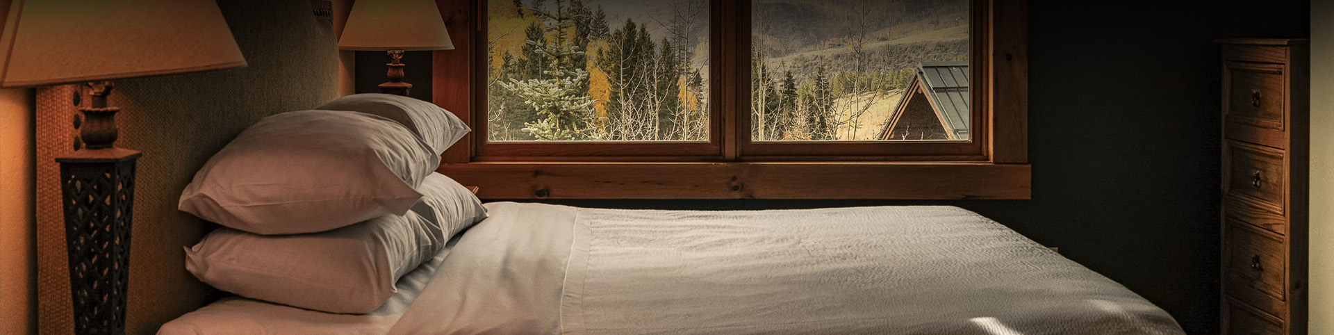 a bed with a white sheet and a window with trees outside