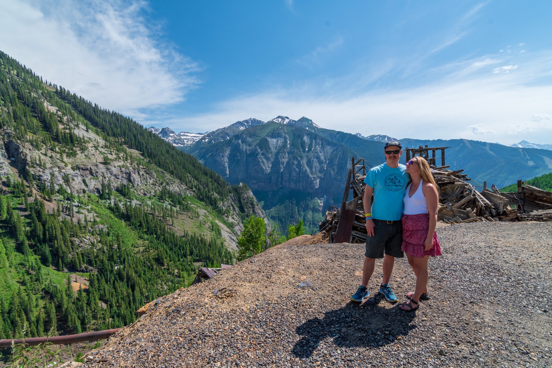 a man and woman standing on a rocky hill with mountains in the background