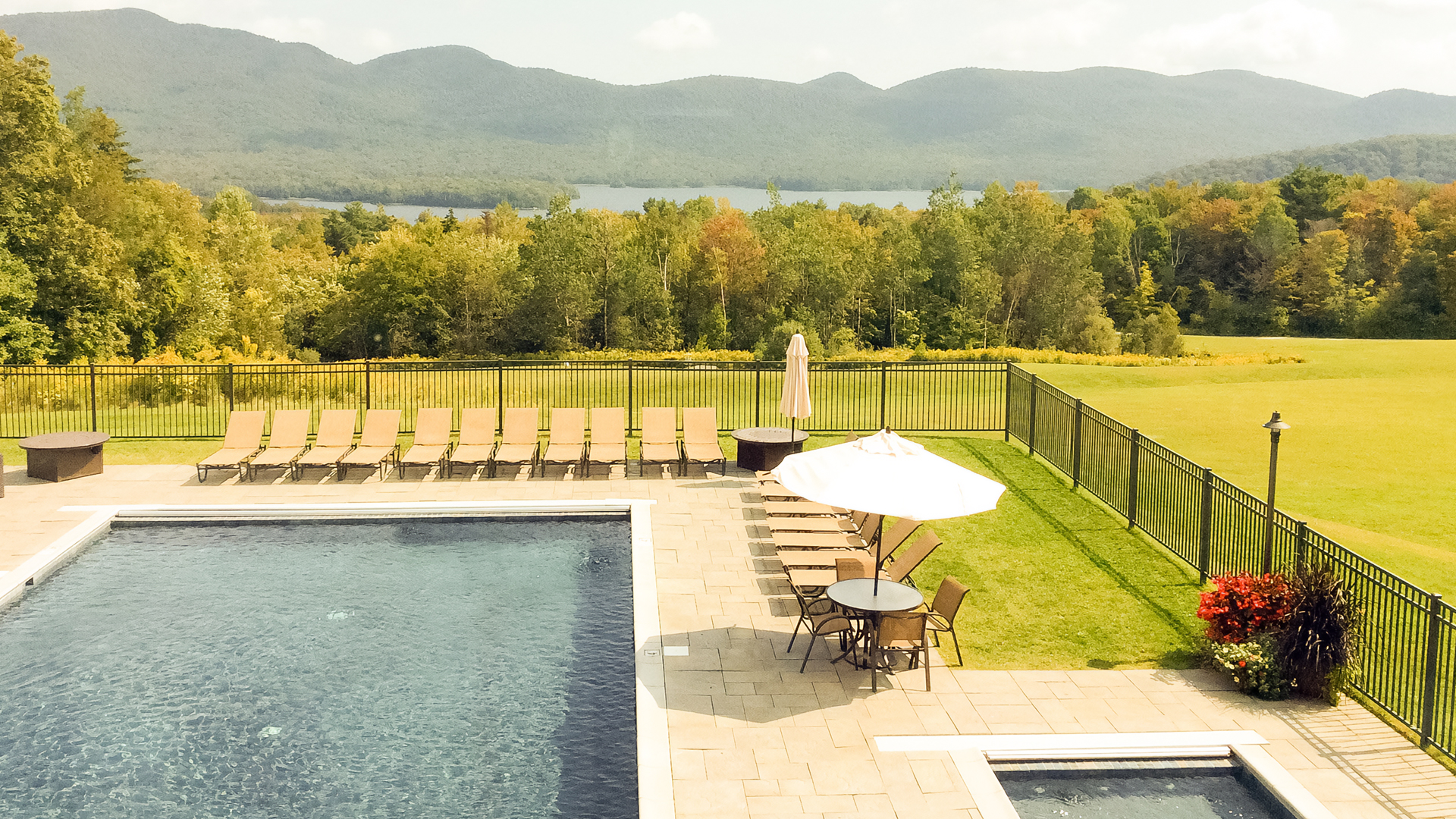 a pool with chairs and a fence and a lawn with mountains in the background