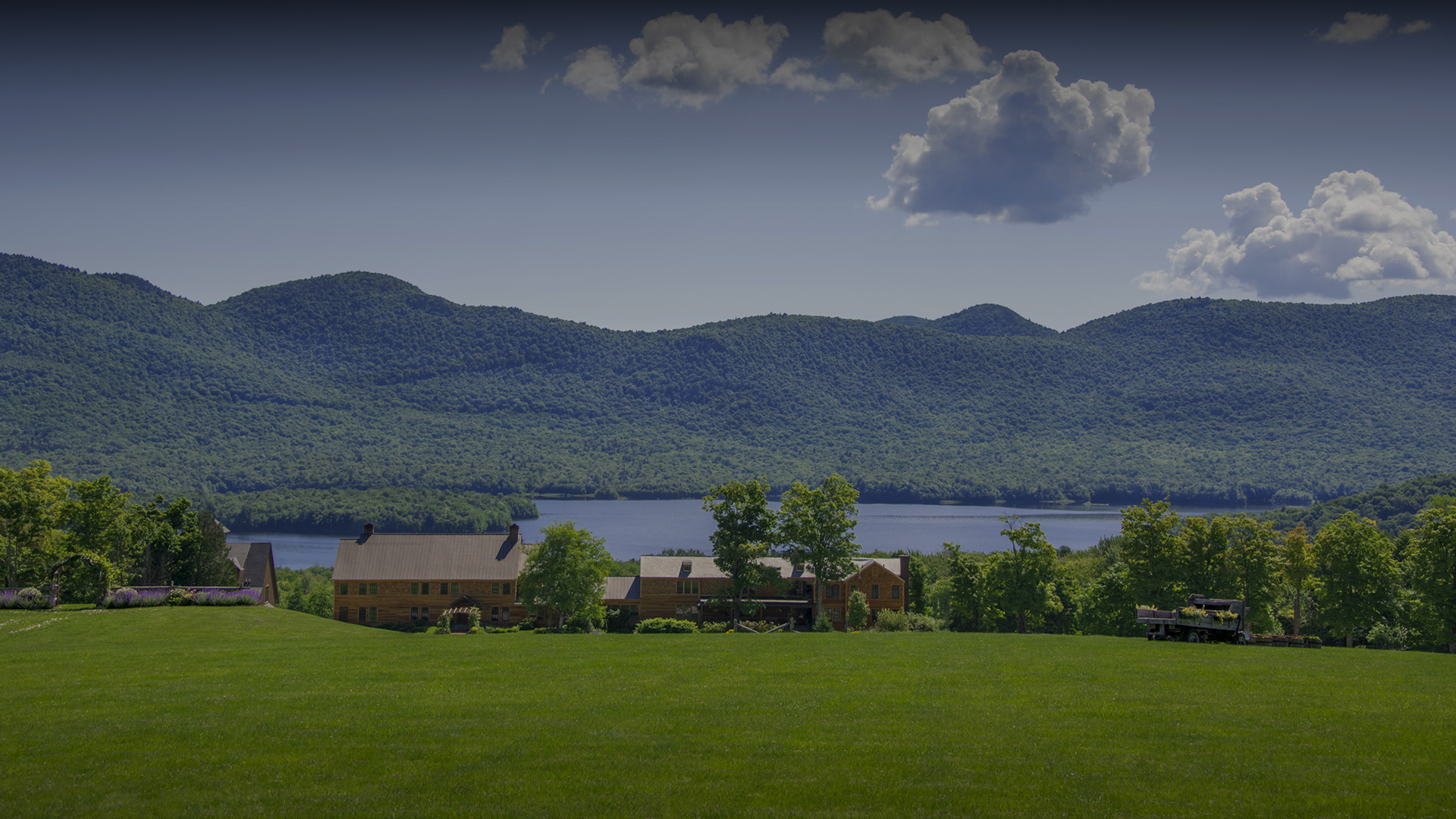 a house in a grassy field with a lake and mountains in the background
