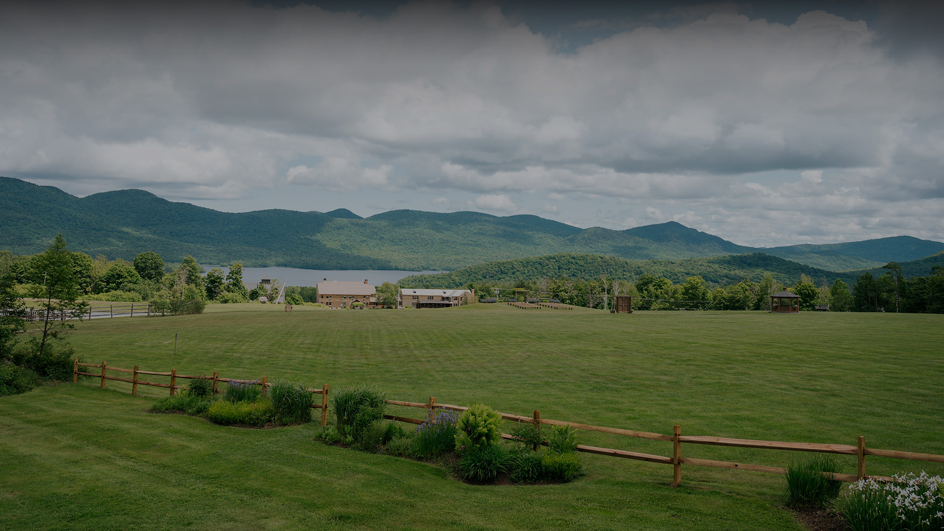 a large grassy field with a fence and mountains in the background