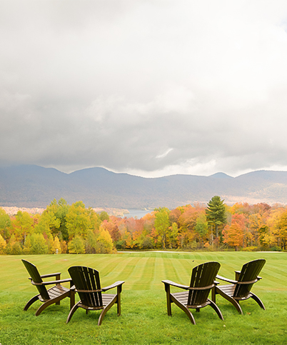 a lawn chairs in a grassy area with trees and mountains in the background