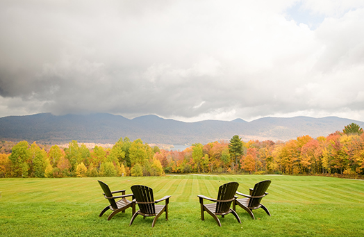 a group of chairs in a grassy field with trees in the background
