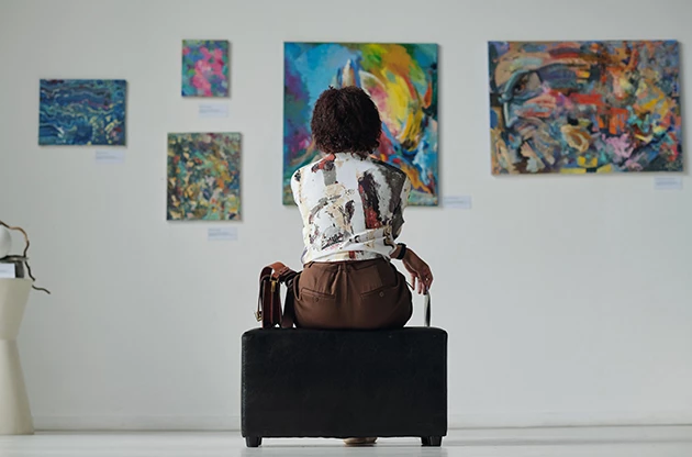 a woman sitting on a black bench looking at art