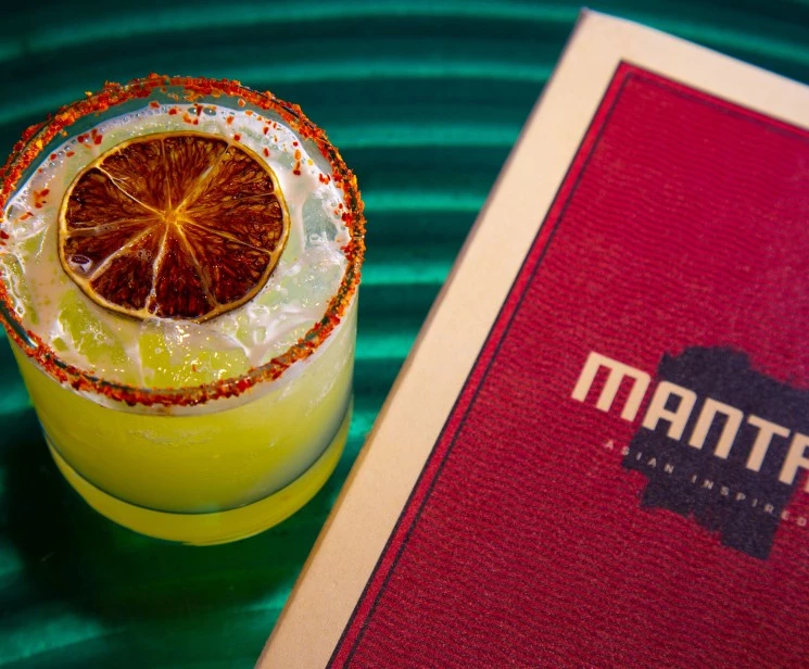 a glass with a slice of orange on top and a book on a green surface