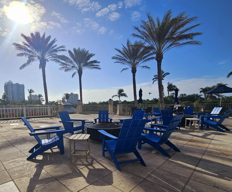 a group of blue chairs and a fire pit on a patio with palm trees