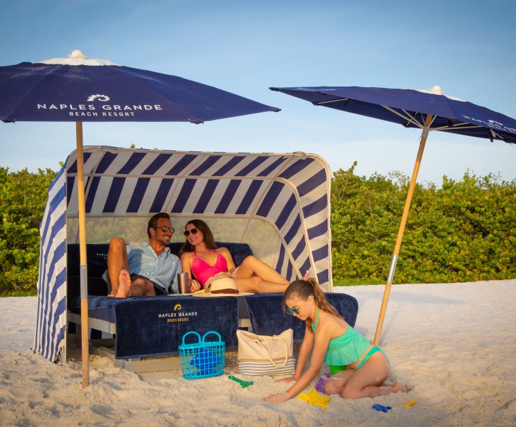 a group of people sitting on a beach bed under umbrellas
