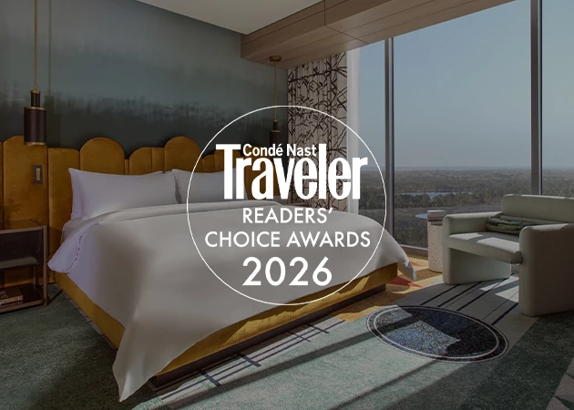 A hotel room with a large bed, chair, and window overlooking a city view.