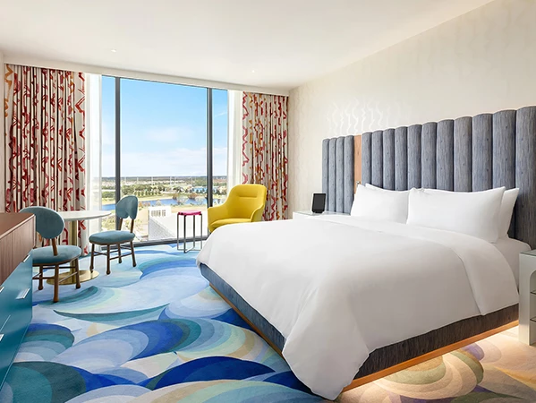 A wide view of a hotel room with a large bed, window, desk, and chairs.