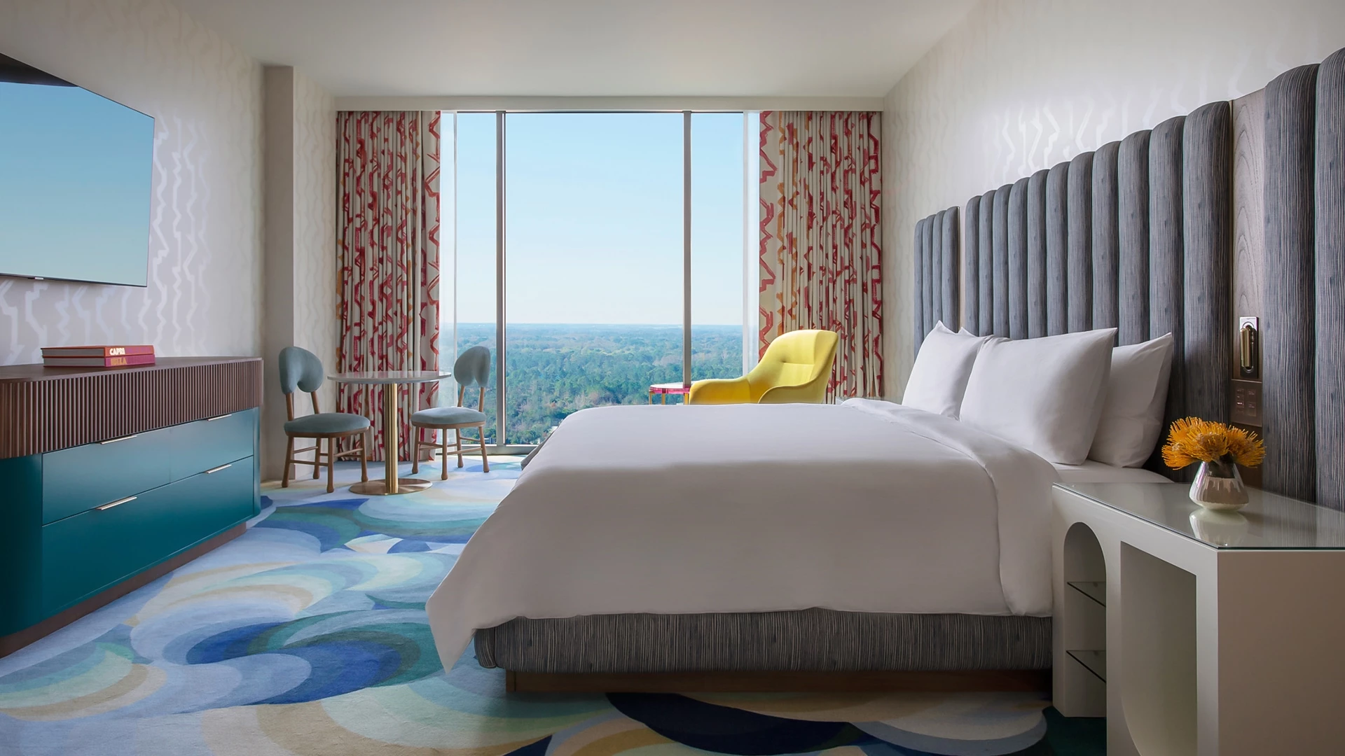 A hotel room with a large bed, TV, table, chairs, and a window with a view.