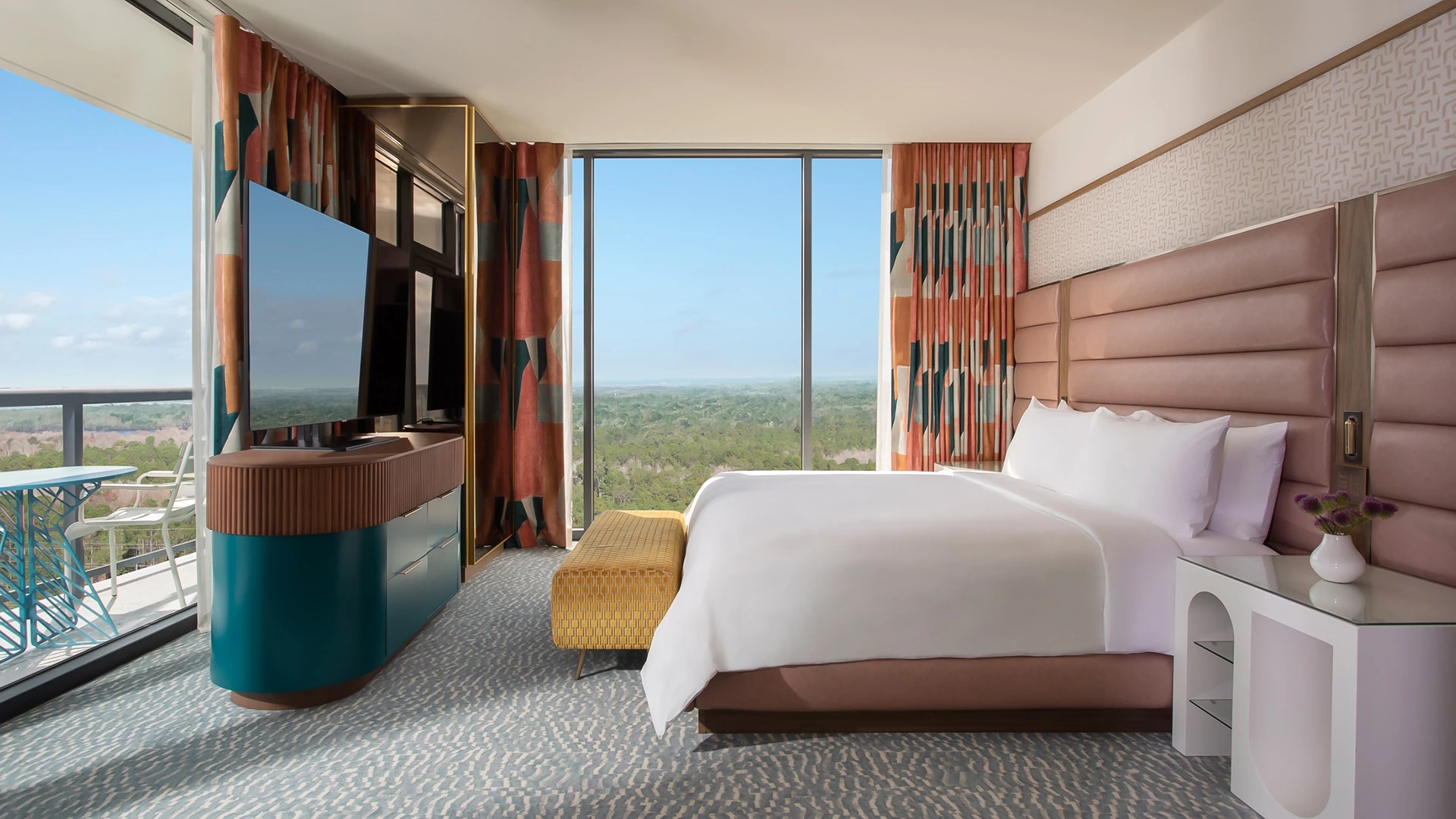 A hotel room with a bed, TV, and balcony with a view.