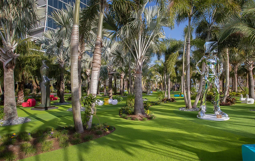a well-manicured lawn with palm trees and modern sculptures