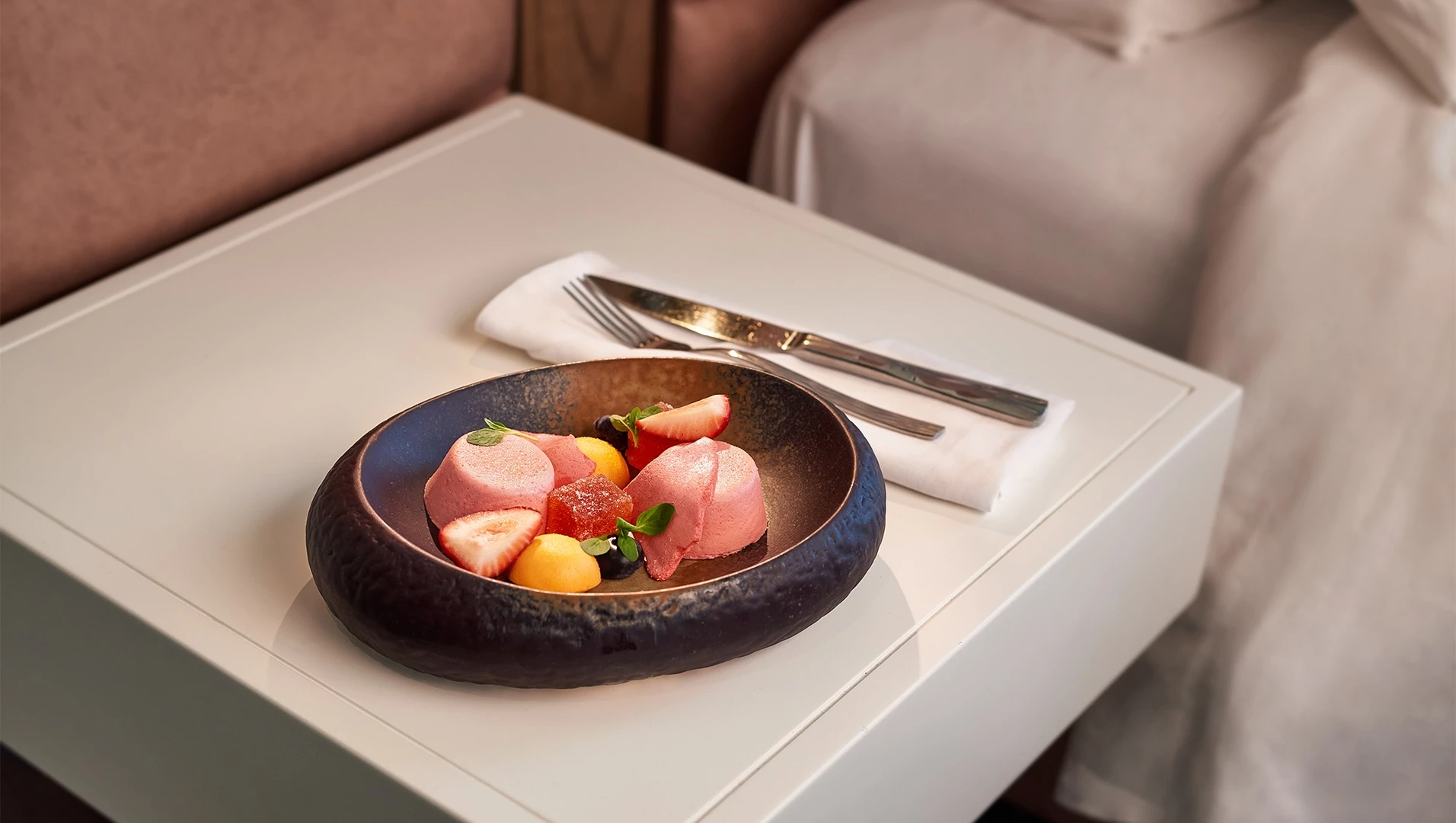 a plate of food on a white table beside a bed