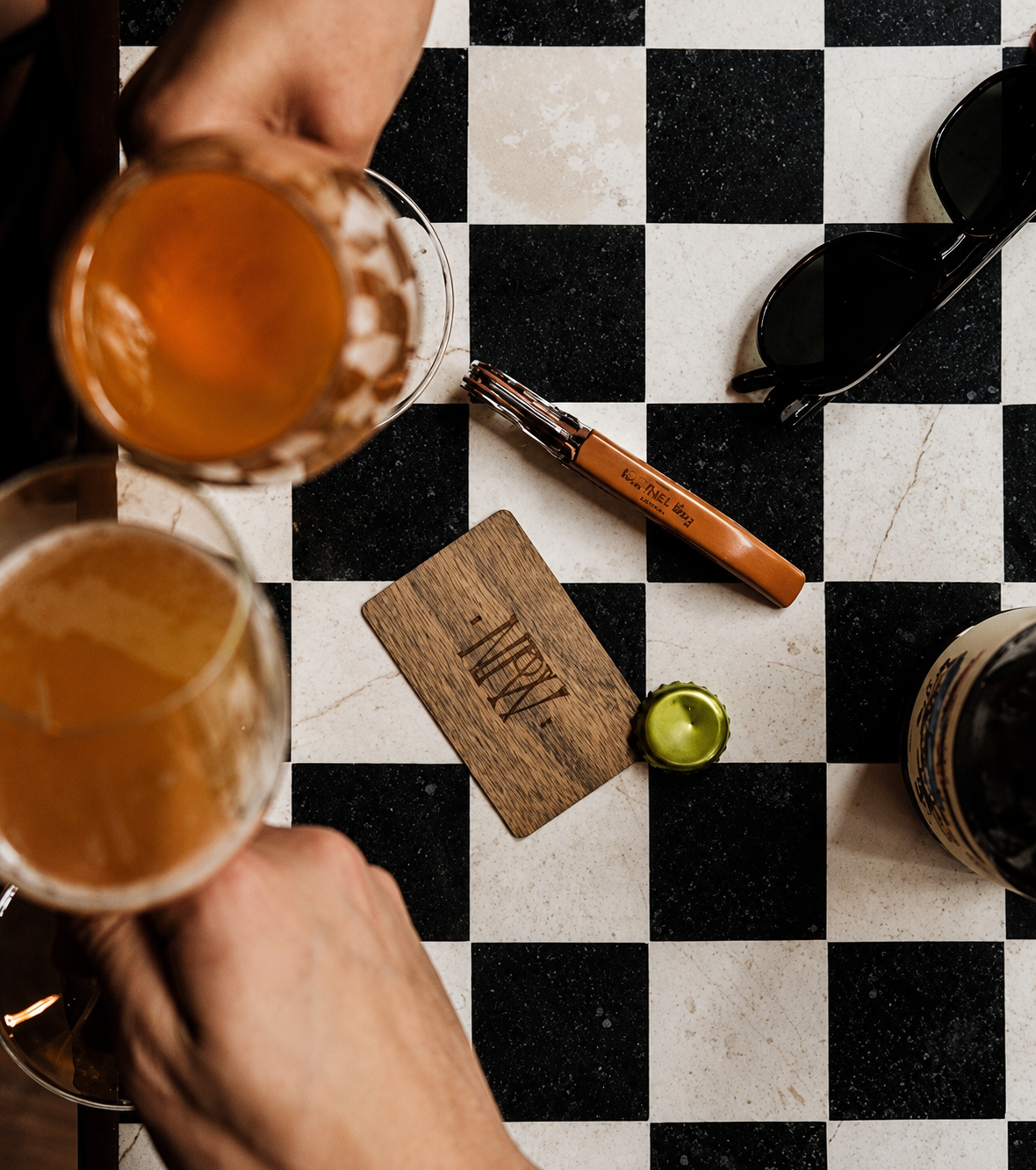 a pair of hands holding glasses of beer on a checkered table