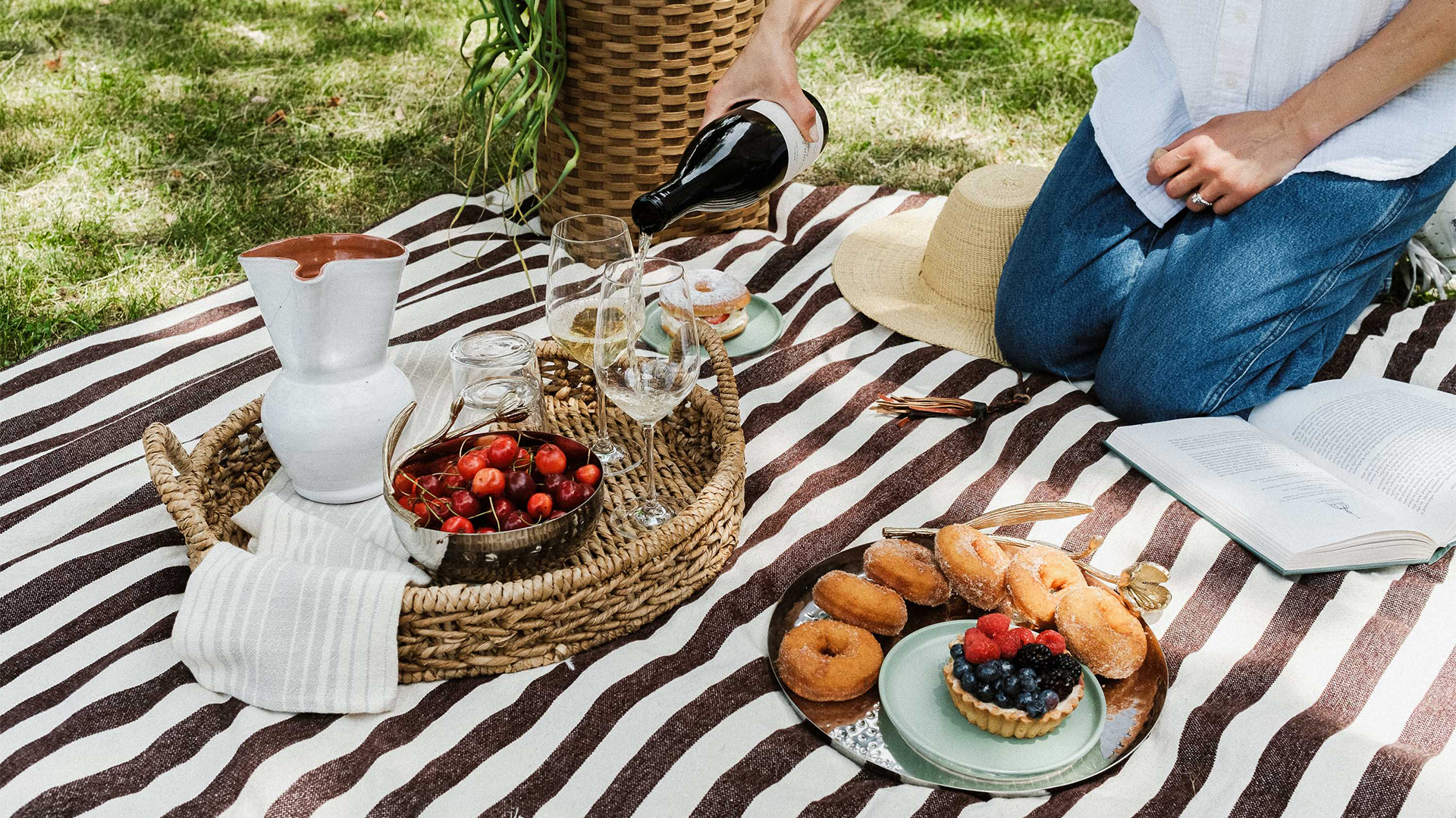 a person pouring wine into glasses on a picnic blanket