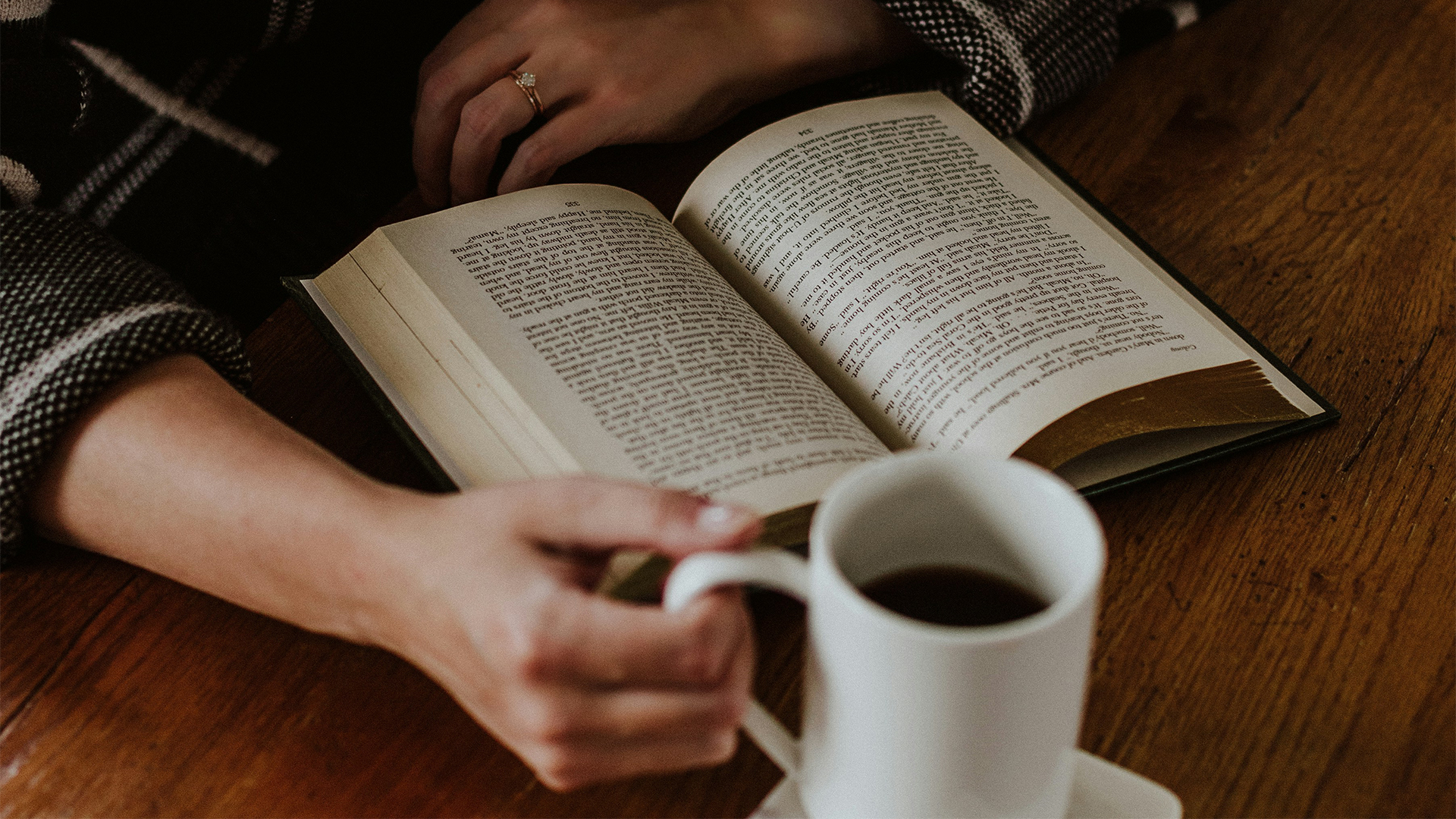 a person holding a cup of coffee next to a book