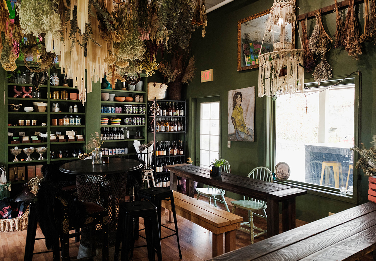 a room with tables and chairs and shelves with bottles and plants from the ceiling