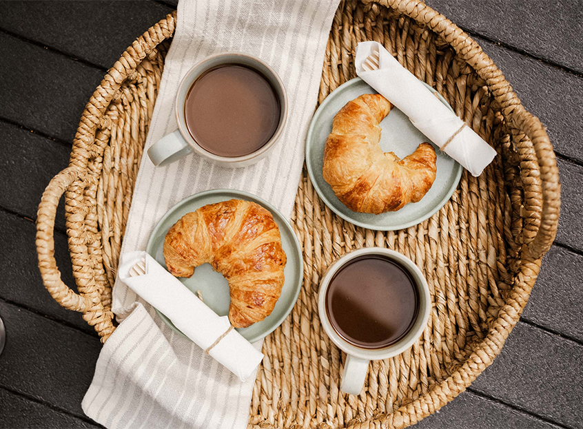 a basket of food with croissants and coffee