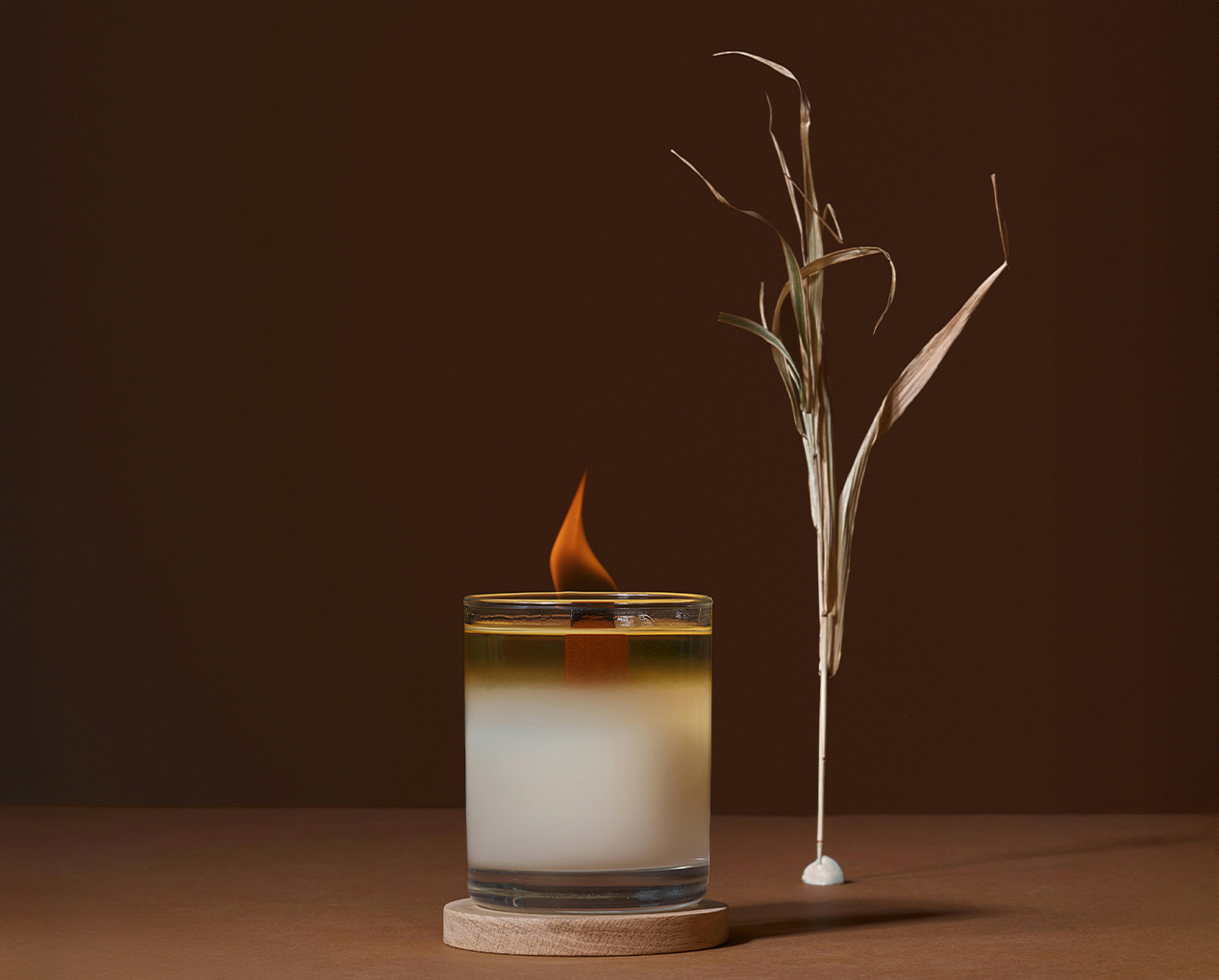 a candle in a glass with a flame next to a plant