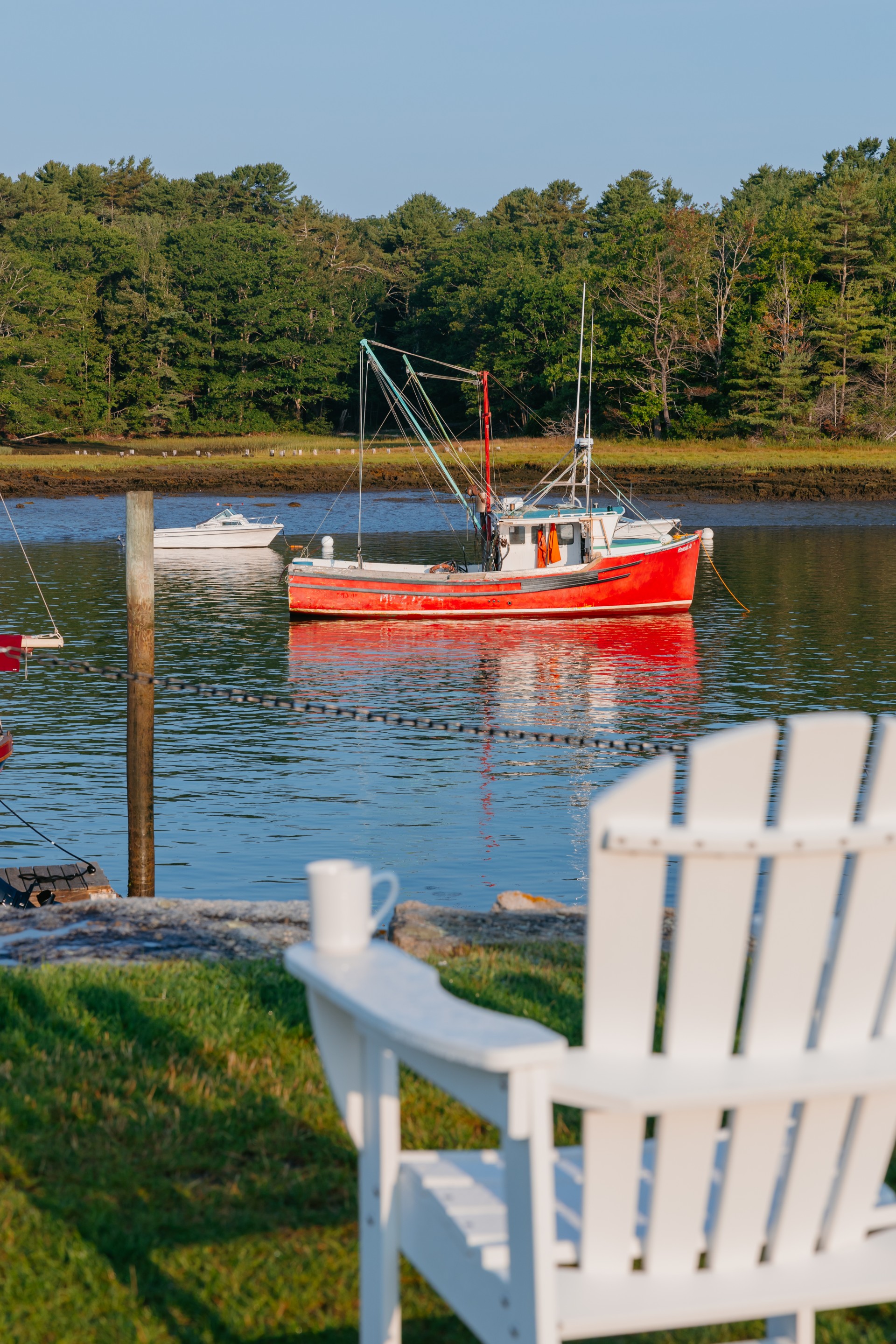 a red boat in a body of water with a white chair and trees