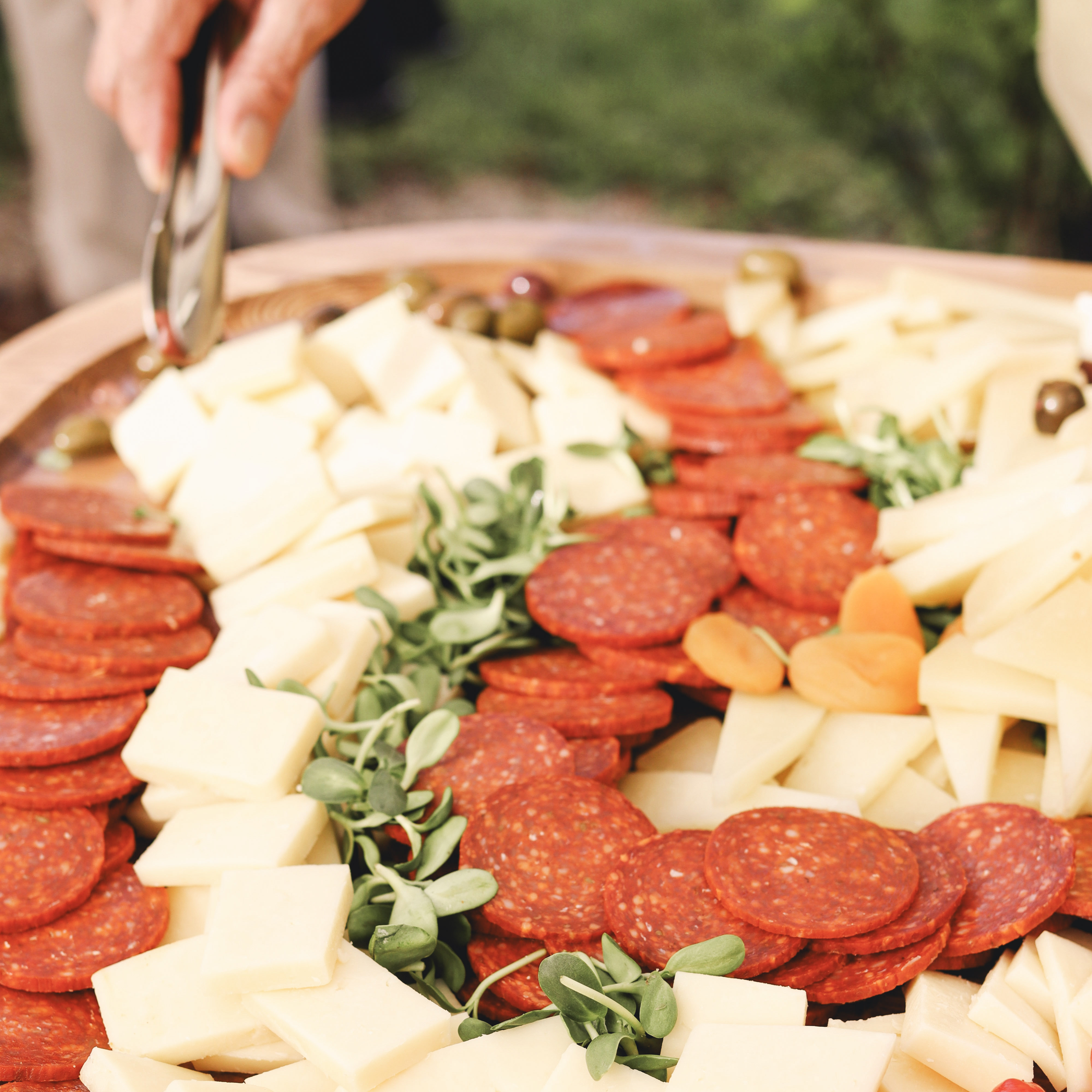 a person cutting a platter of cheese and meat