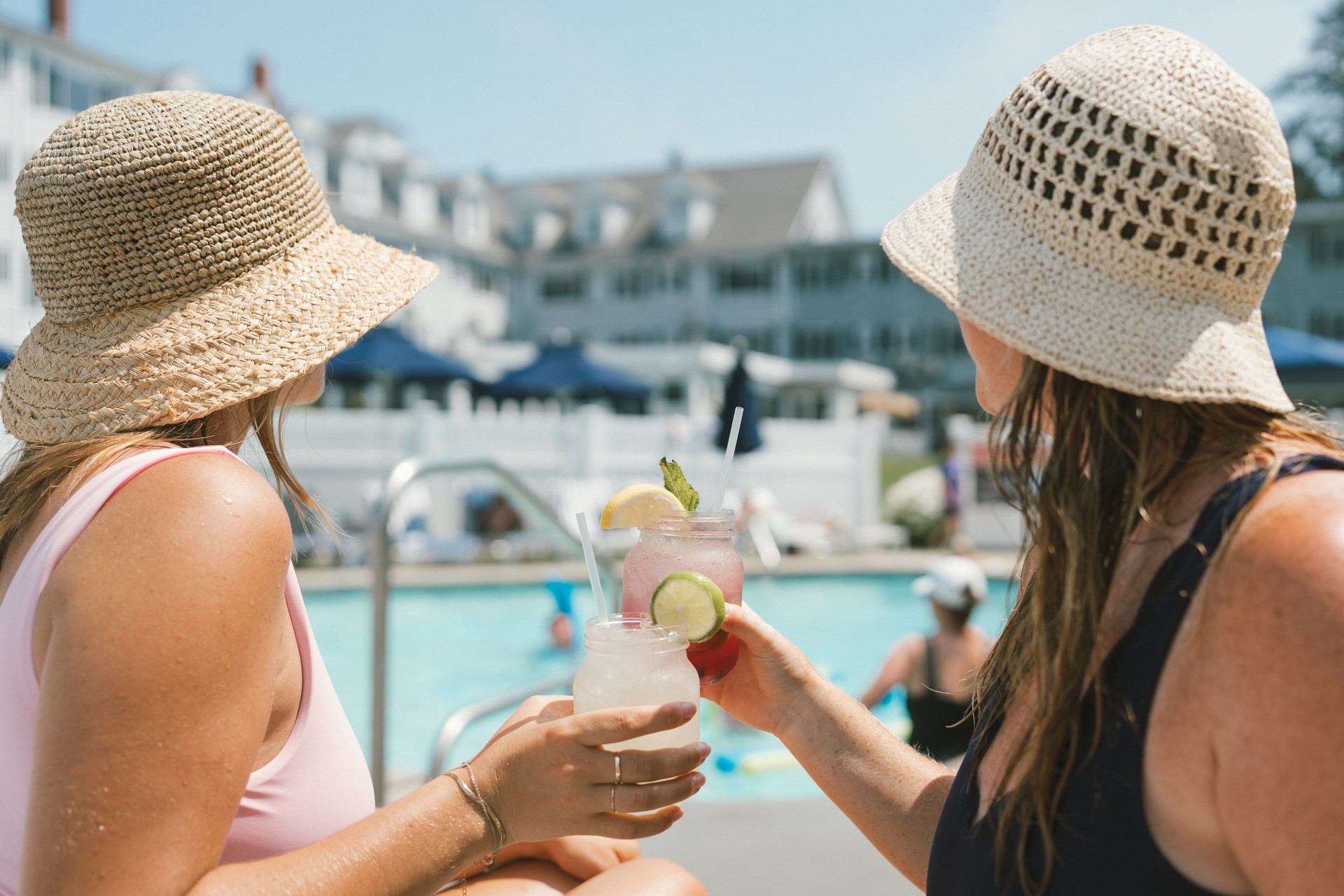 two women holding drinks by a pool