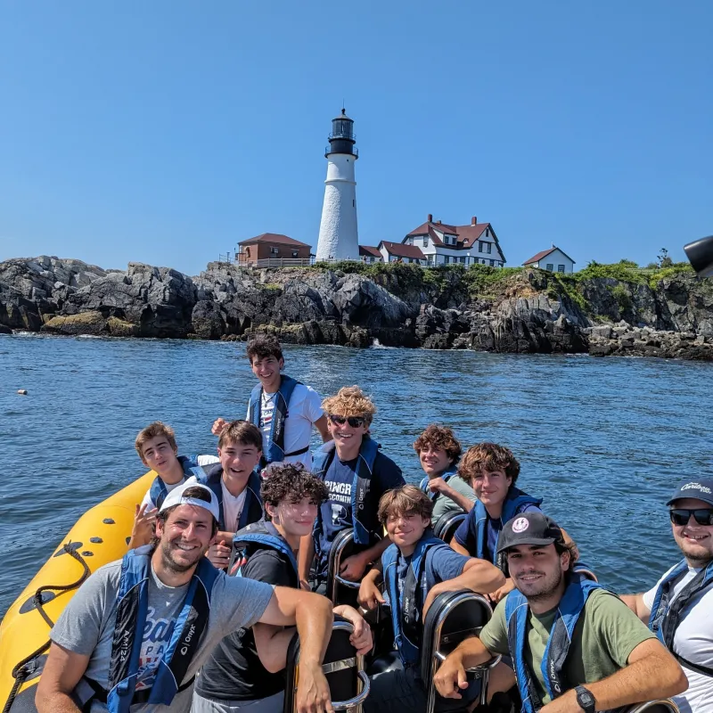 a group of people on a boat in the water with a lighthouse in the background