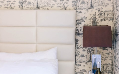 a bed with a lamp and wine glasses on a table