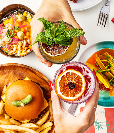 a person holding drinks with food on the table