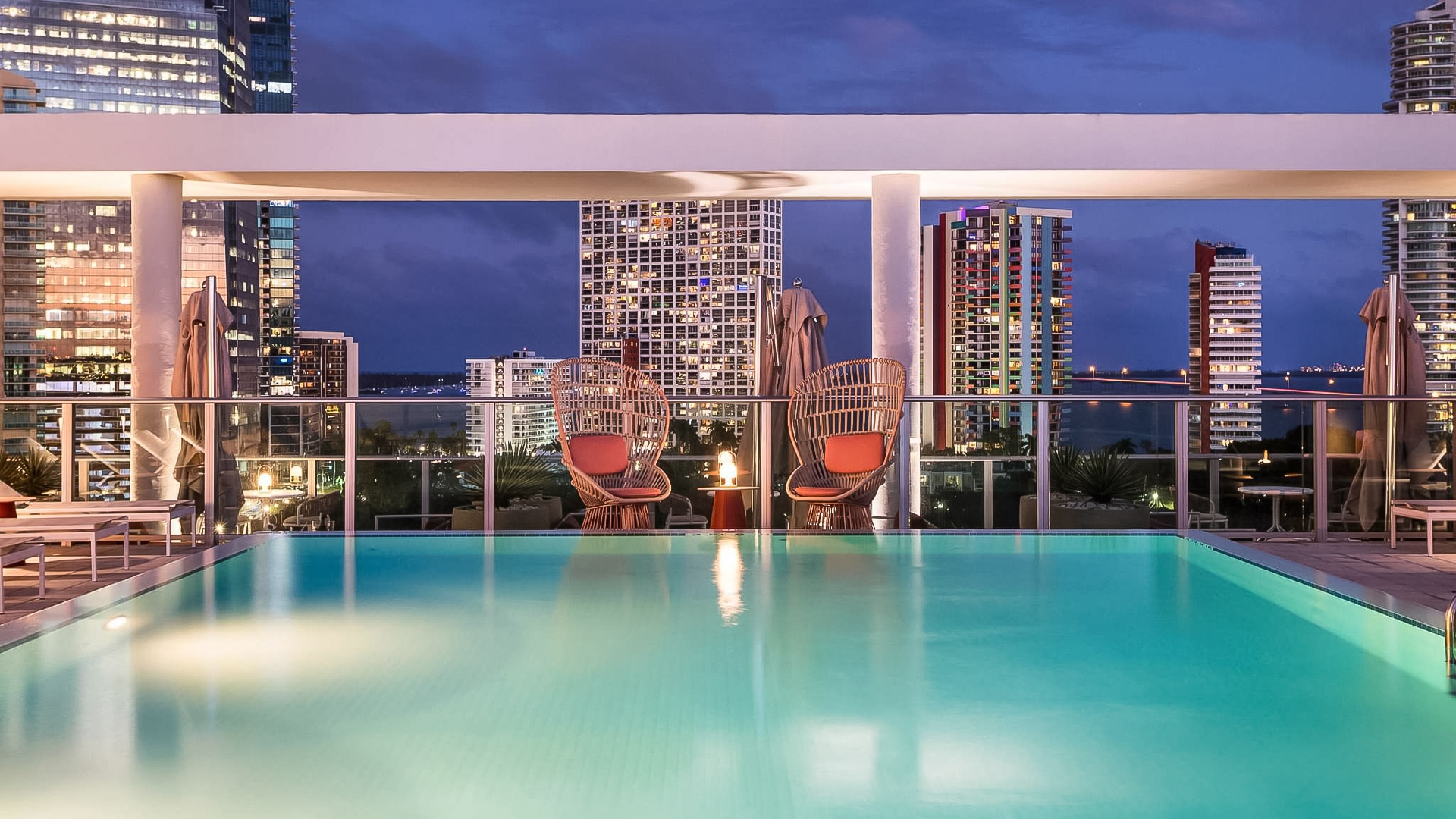 a pool with chairs and a city skyline in the background
