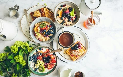 A breakfast spread with bowls of oatmeal, plates of toast, and cups of coffee on a white table.