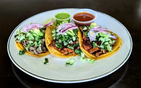 a plate of three tacos with sauce and onions
